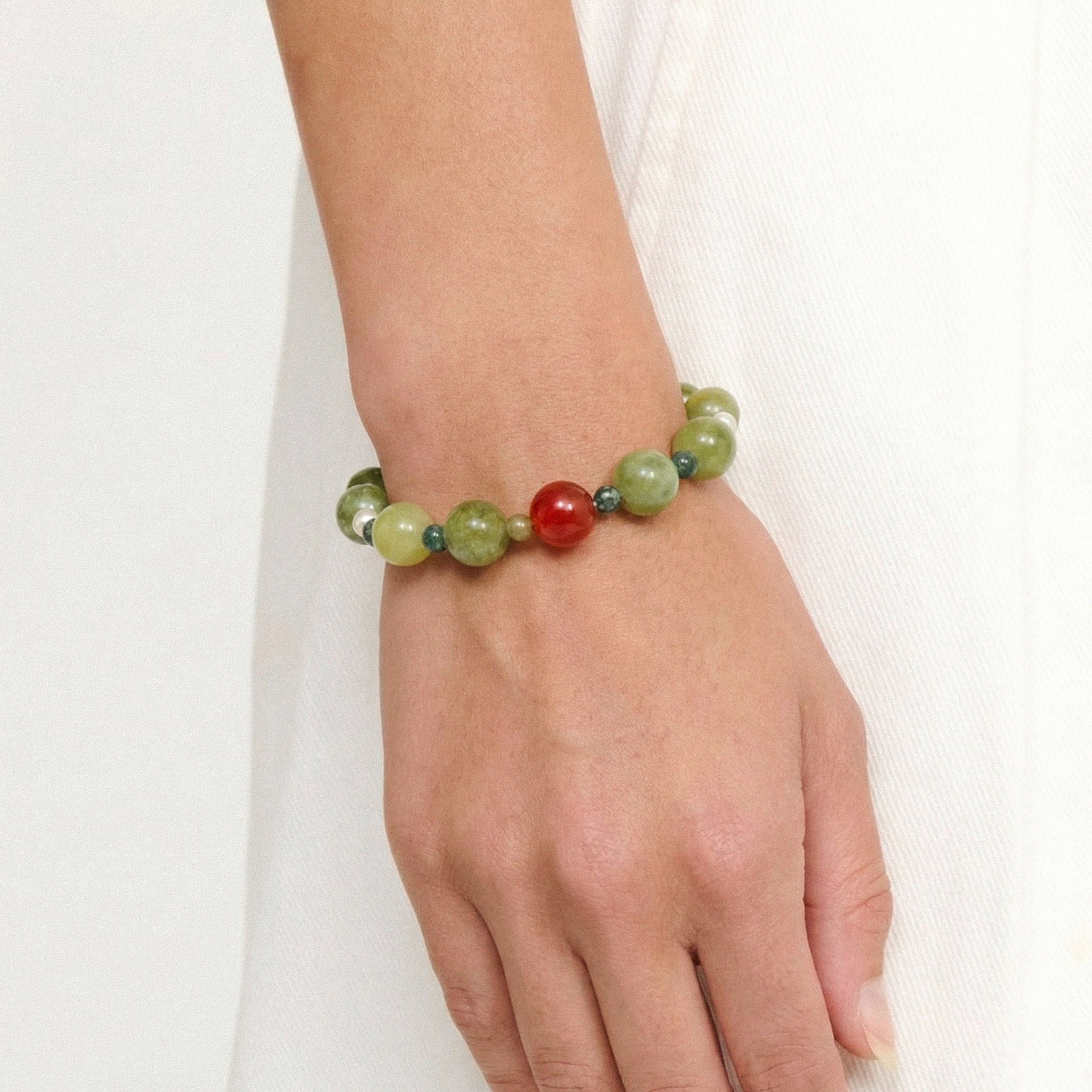 Beaded bracelet with green and red beads on a wrist against a white background